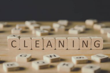 selective focus of word cleaning made of cubes surrounded by blocks with letters on wooden surface isolated on black clipart