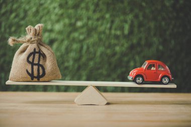 yeşil arka plan üzerinde tahterevalli üzerinde dengeleme dolar işareti ile oyuncak araba ve para çantası