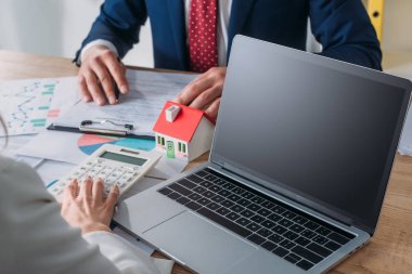 yakın dizüstü bilgisayar, ev modeli, grafikler ve grafikler ile işyerinde otururken hesap makinesi kullanarak kredi anlaşması ve iş kadını eğitimi adam kırpılmış çekim