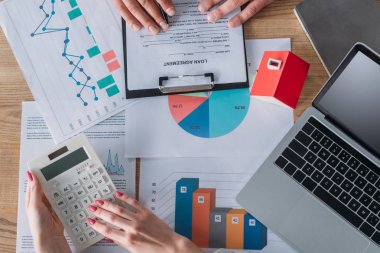 dizüstü bilgisayar, ev modeli, grafikler ve grafikler yakınında işyerinde otururken hesap makinesi kullanarak adam okuma kredi anlaşması ve iş kadını kırpılmış çekim