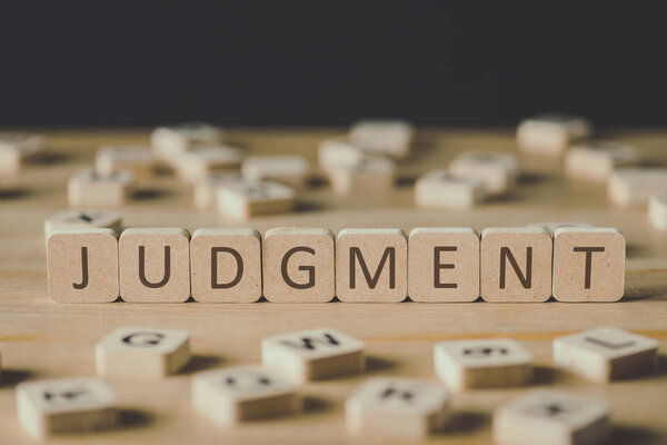selective focus of cubes with word judgement surrounded by blocks with letters on wooden surface isolated on black