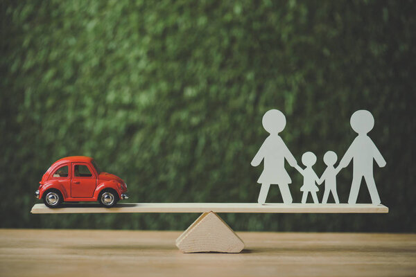 red miniature car and paper cut family balancing on swing on green background