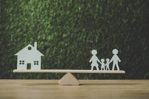 paper cut house and paper family balancing on seesaw on green background