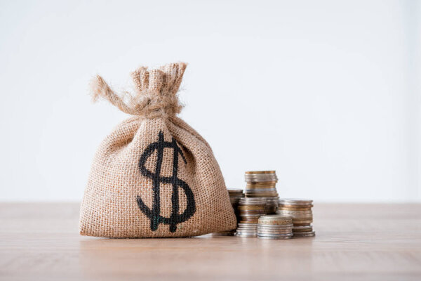 money bag with dollar sign and stacks of metal coins on wooden surface isolated on grey