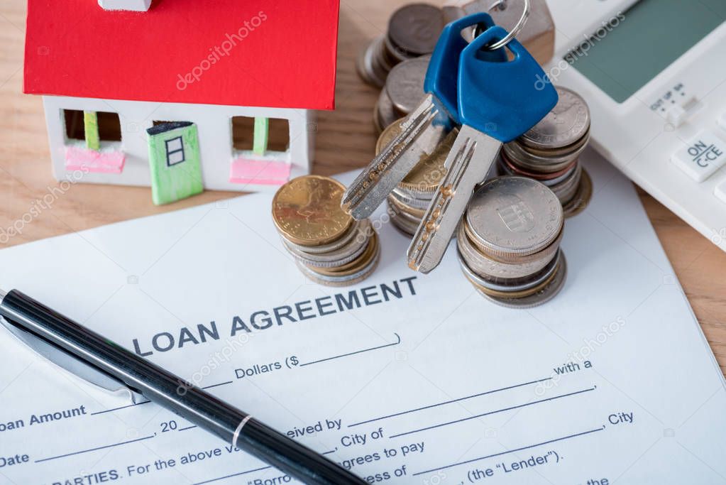 loan agreement, pen, coins, house model and keys on wooden surface