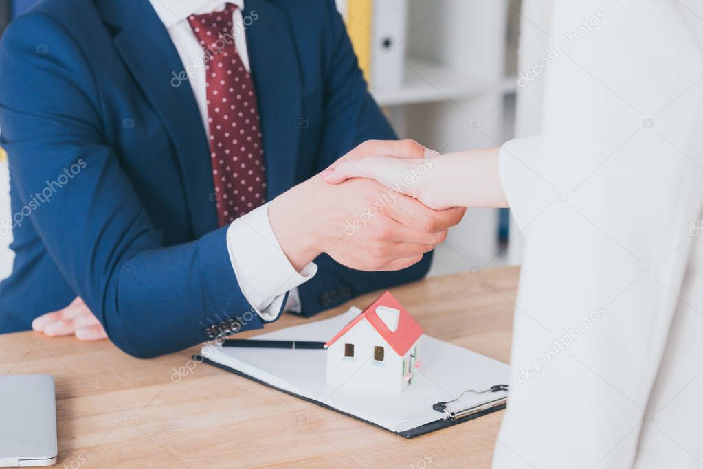 partial view of customer shaking hands with realtor near house model