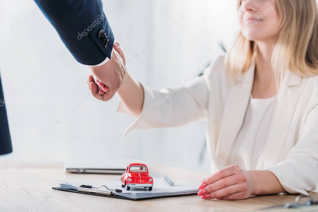 cropped shot of smiling woman shaking hands with businessman near red toy car 