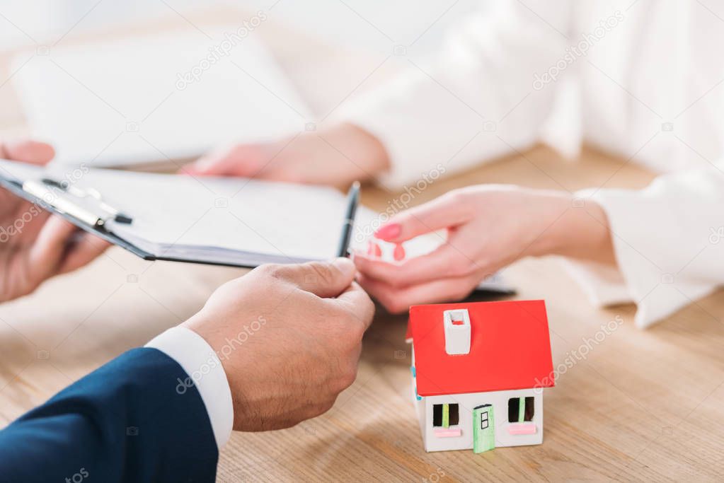 Cropped view of businessman giving clipboard with loan agreement to client near house model