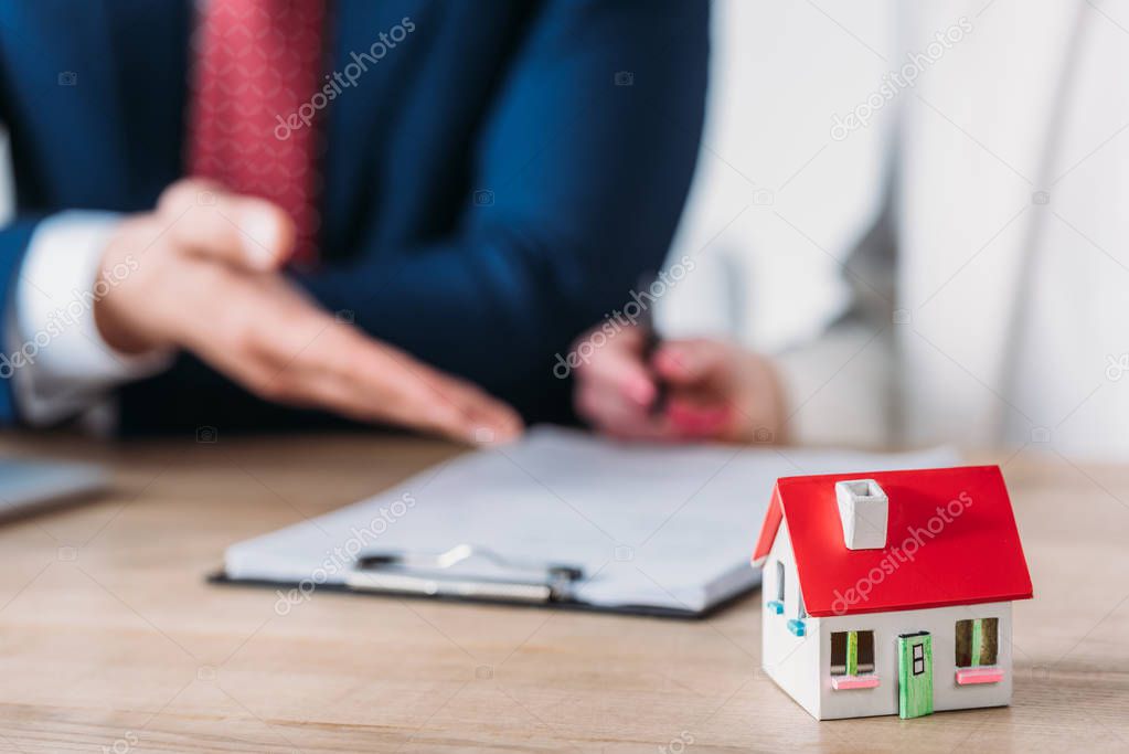 partial view of businessman showing signature place in loan agreement to client holding pen near house model