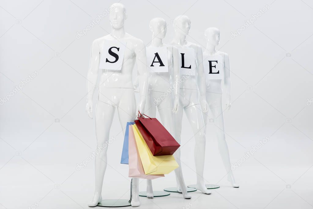 white mannequins with sale lettering on papers and shopping bags on grey