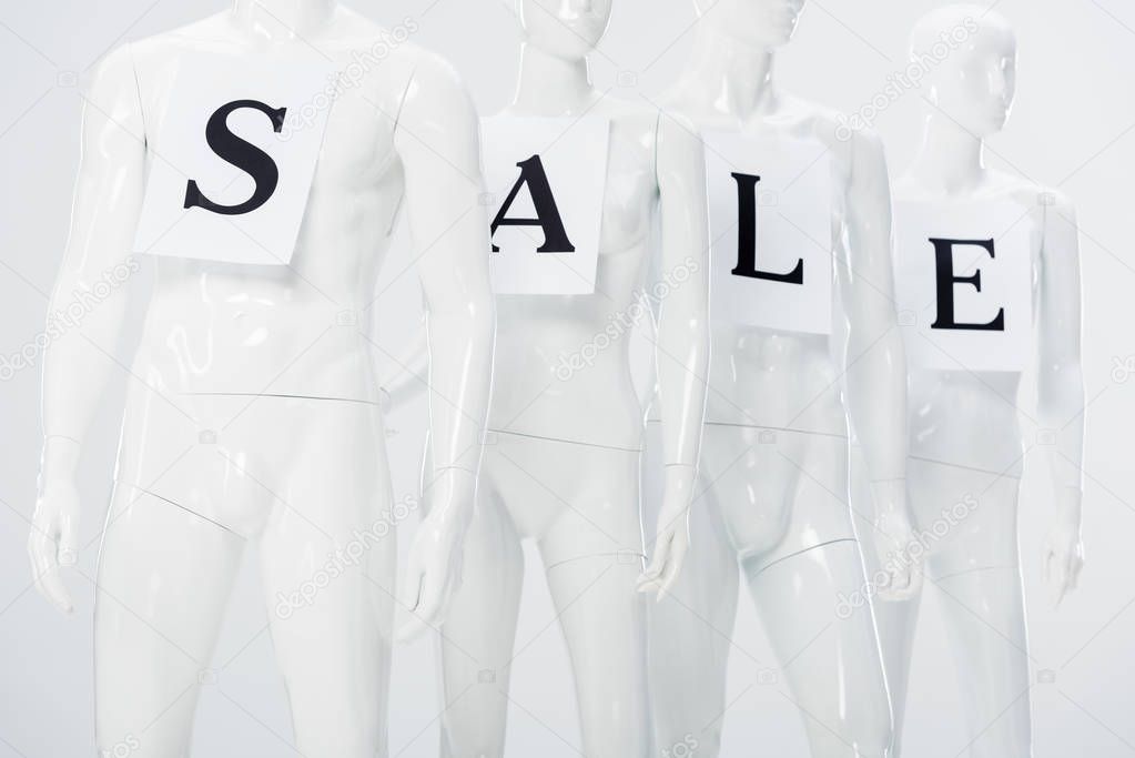 papers with sale lettering on white plastic mannequins on grey