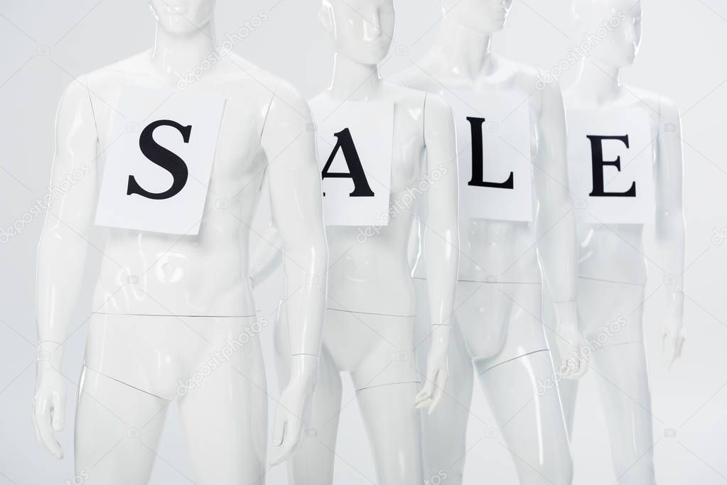 papers with sale lettering on white plastic mannequins isolated on grey