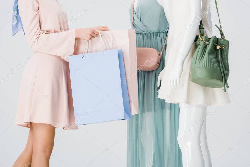 partial view of young woman holding shopping bags near mannequins isolated on grey