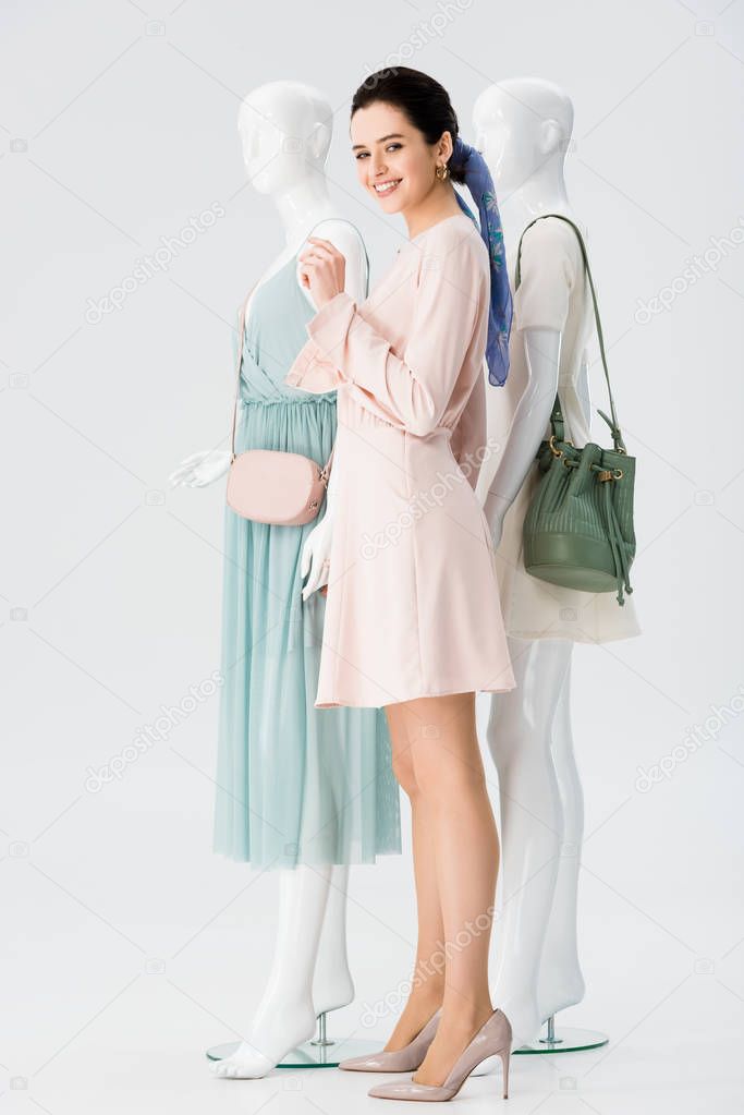 beautiful smiling girl posing with mannequins in dresses isolated on grey
