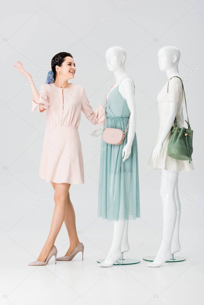 beautiful smiling young woman posing near mannequins in dresses on grey