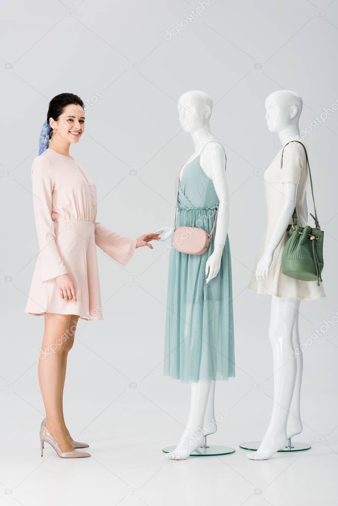 beautiful smiling girl looking at camera near mannequins in dresses on grey