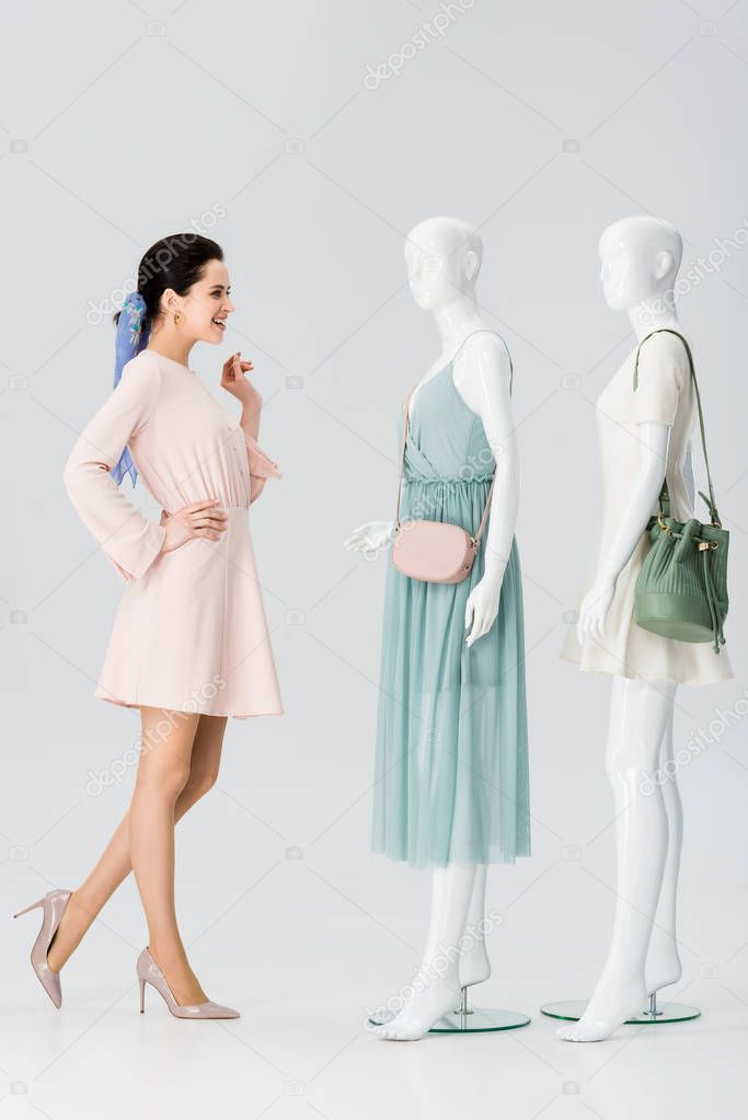 beautiful smiling girl looking at mannequins in dresses on grey