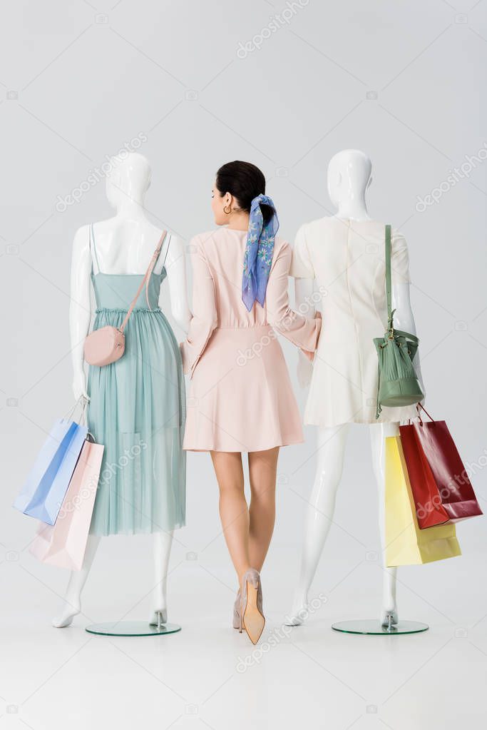 back view of young woman holding hands with mannequins with shopping bags isolated on grey