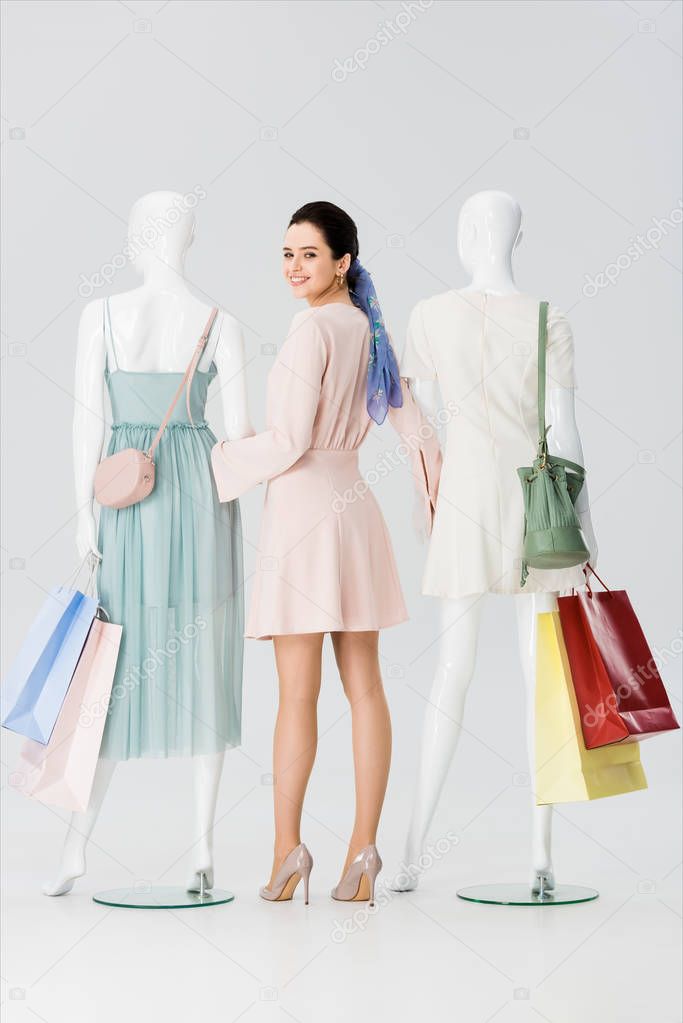 beautiful young woman holding hands with mannequins with shopping bags isolated on grey