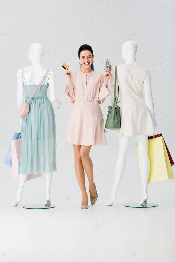 girl with credit card and money near mannequins with shopping bags on grey