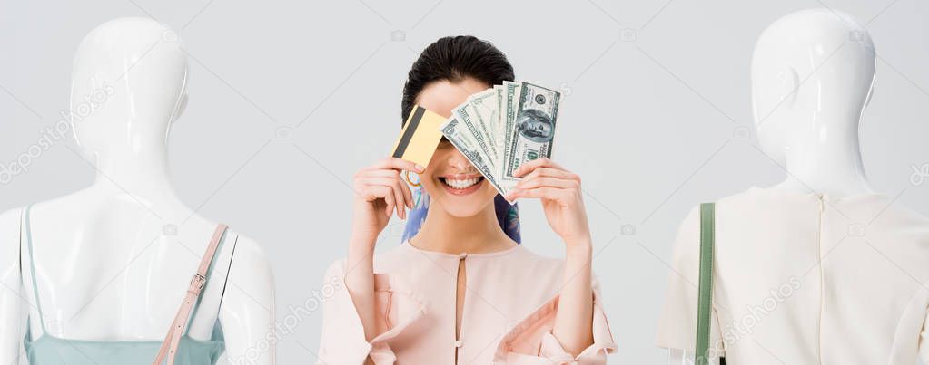 panoramic shot of girl near mannequins covering face with money and credit card isolated on grey