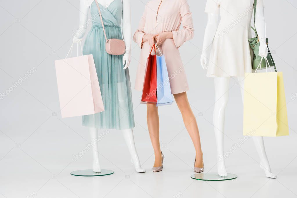 cropped view of young woman with shopping bags near mannequins on grey