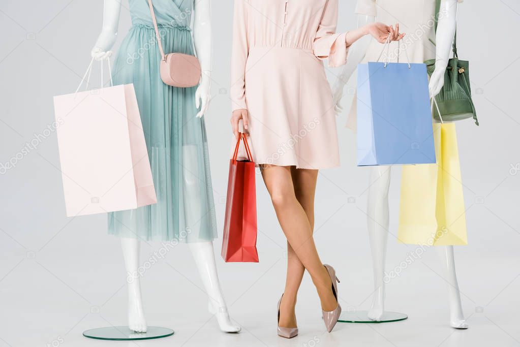 partial view of girl with shopping bags near mannequins on grey