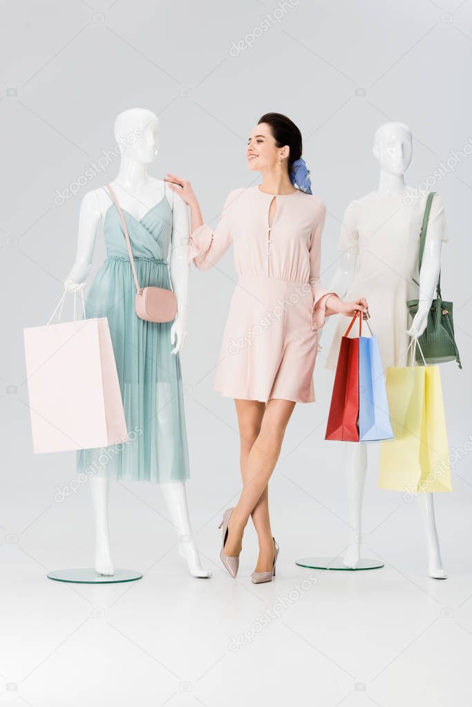 beautiful girl with shopping bags near mannequins on grey