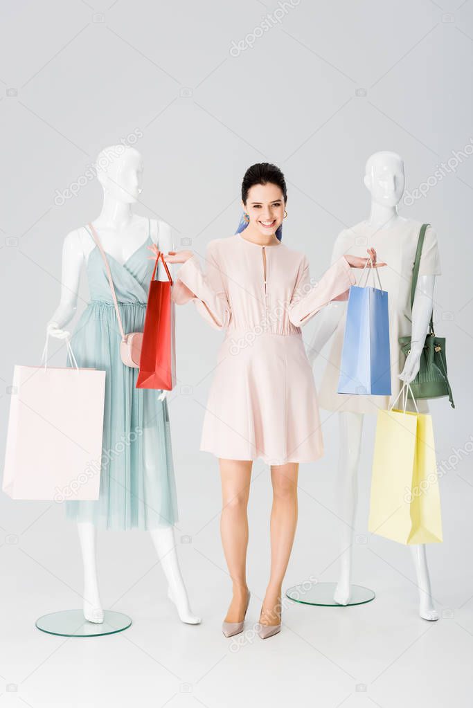 beautiful happy girl with shopping bags near mannequins on grey