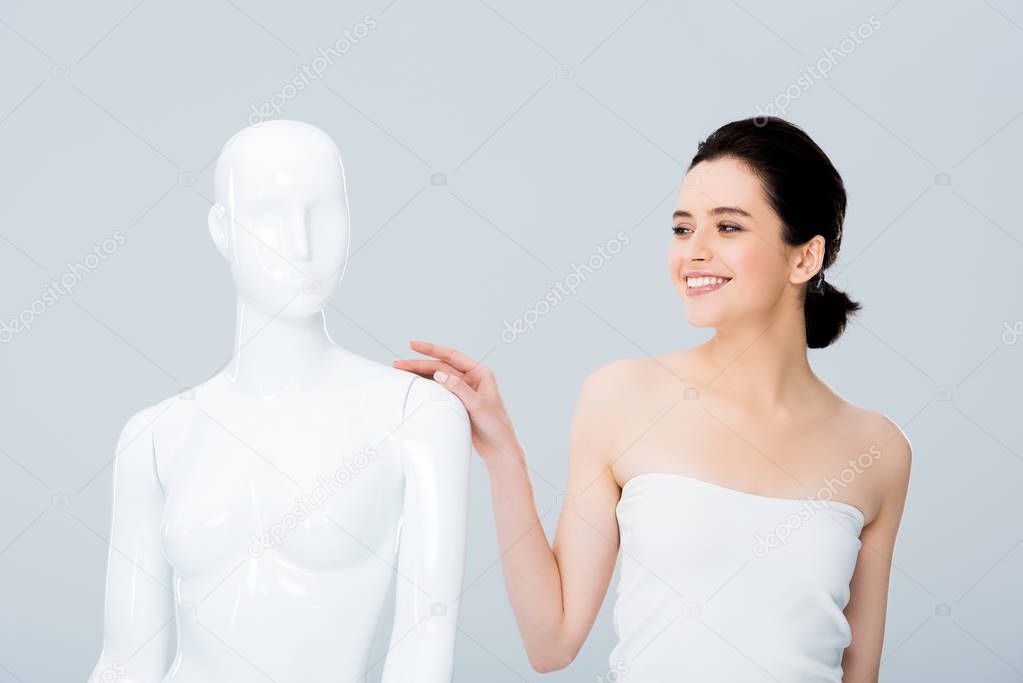 attractive smiling young woman in white posing with mannequin isolated on grey