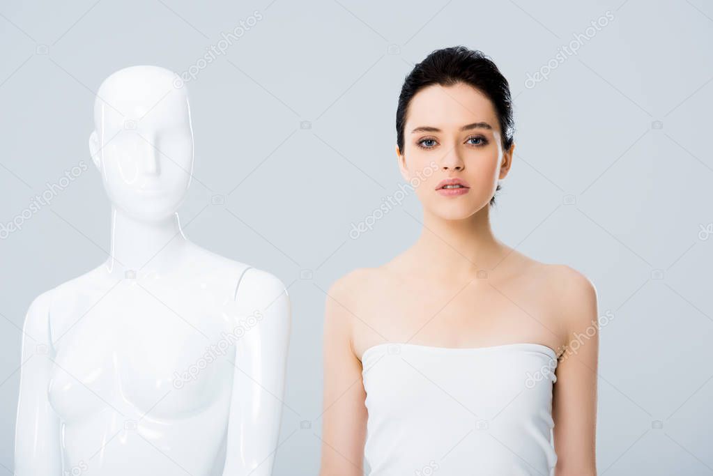attractive young woman in white posing with mannequin isolated on grey