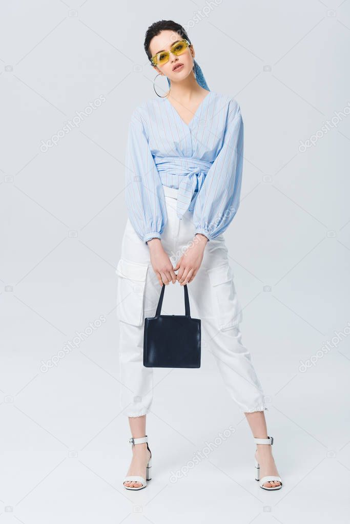 beautiful stylish girl with bag looking at camera and posing on grey