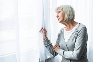 sad senior woman with grey hair looking at window clipart