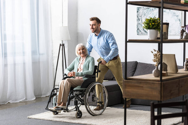 smiling man carrying disabled senior mother on wheelchair