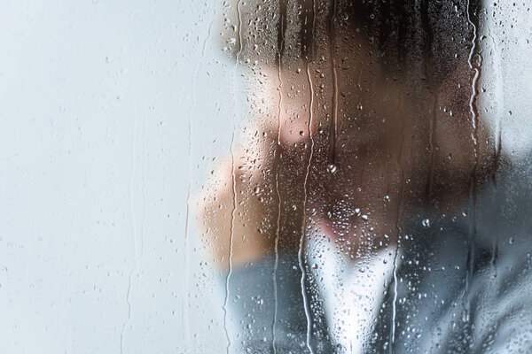 selective focus of crying man behind wet window