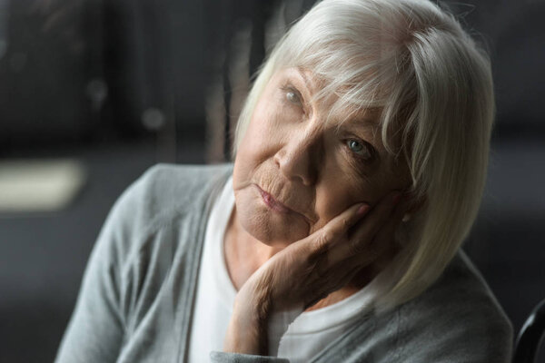 selective focus of pensive senior woman with grey hair propping face with hand
