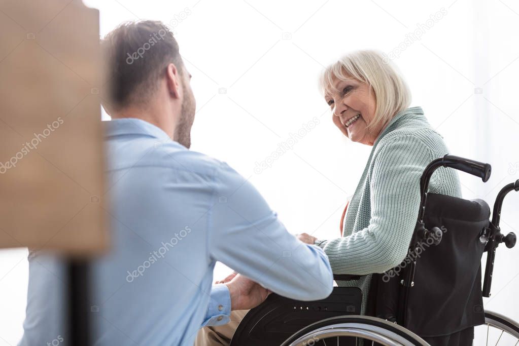 back view of man near disabled senior mother at home