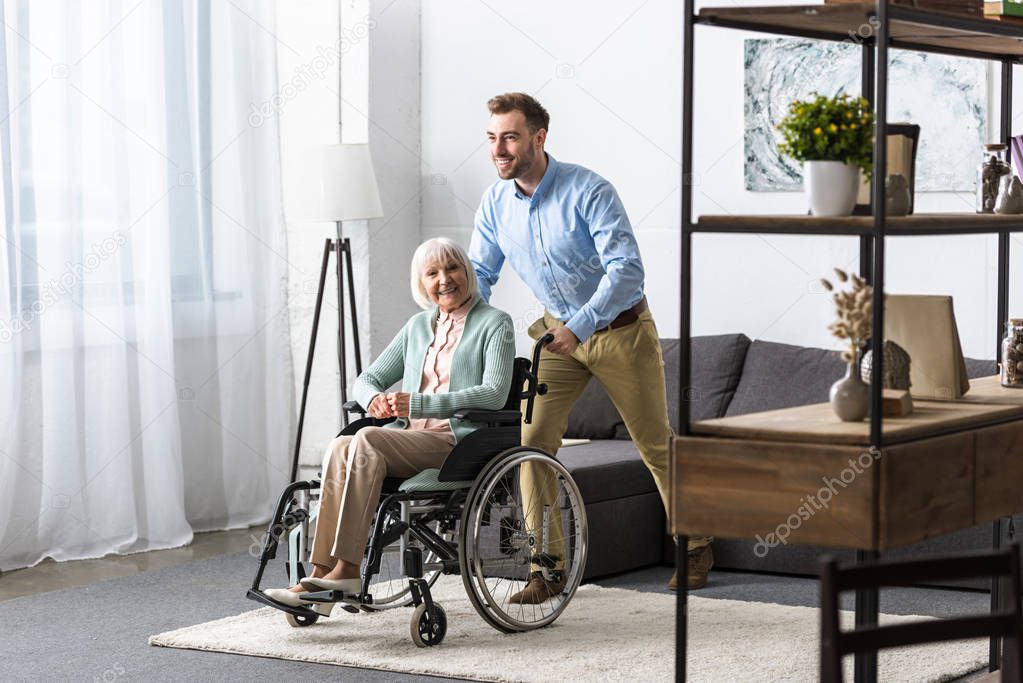 smiling man carrying disabled senior mother on wheelchair