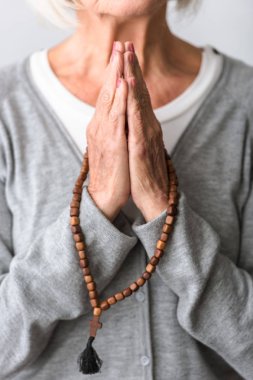 partial view of senior woman praying with wooden rosary clipart