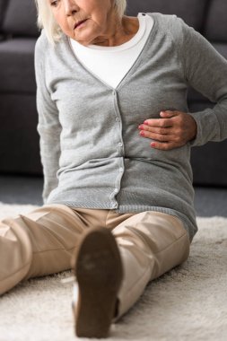 halı üzerinde oturan kalp krizi olan yaşlı kadının kısmi görünümü