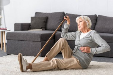 suffering senior woman with heart attack sitting on carpet clipart