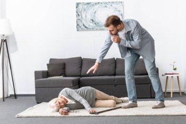 full length view of worried man standing near senior woman lying on carpet clipart