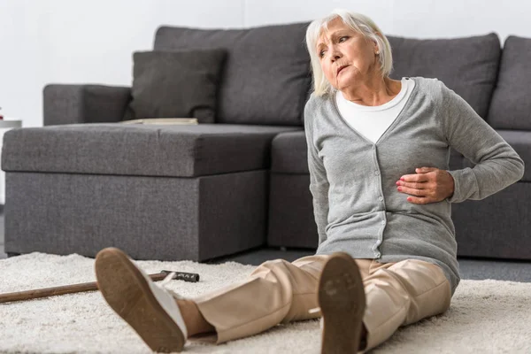 suffering senior woman with heart attack sitting on carpet