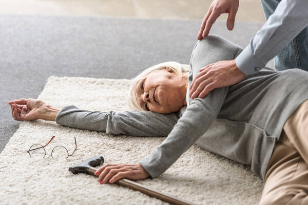 cropped view of man helping senior mother with heart attack fallen on carpet