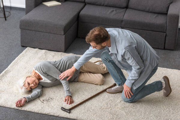 overhead view of adult man with sick senior mother lying on carpet