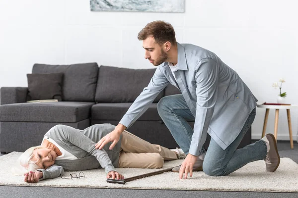 Hombre Preocupado Cerca Mujer Mayor Acostado Alfombra — Foto de Stock