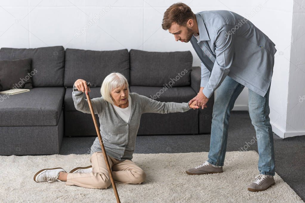 full length view of man helping senior mother fallen on floor