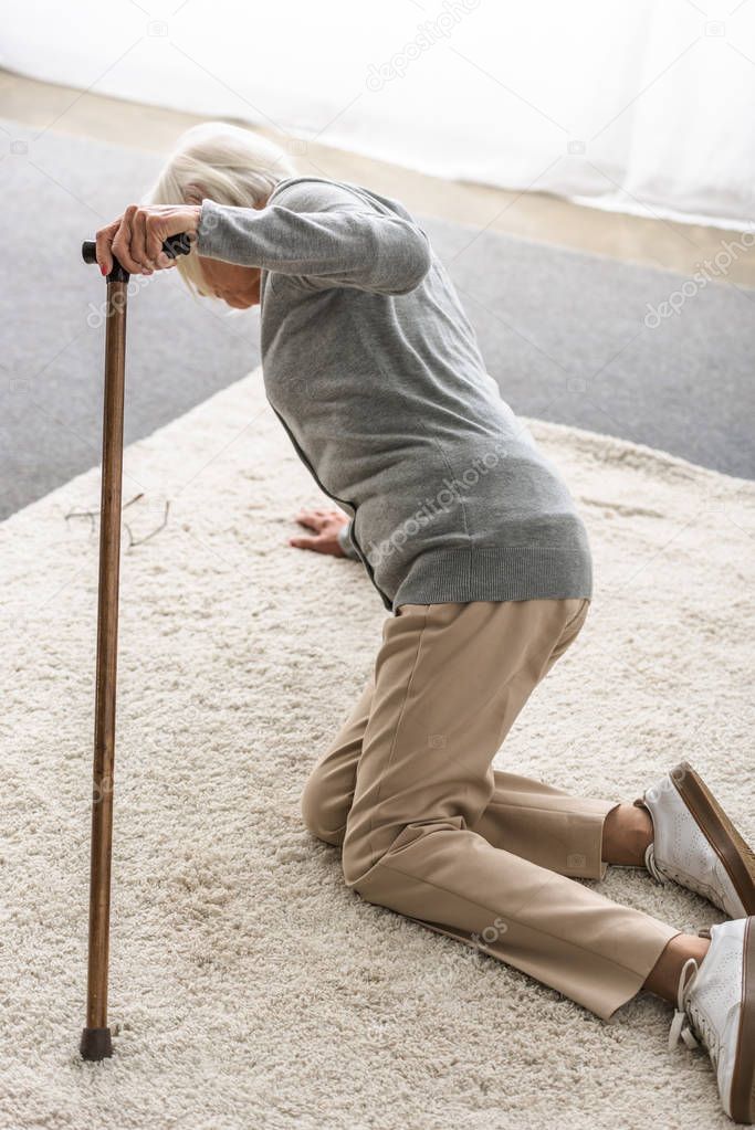 sick senior woman with wooden cane fallen on carpet