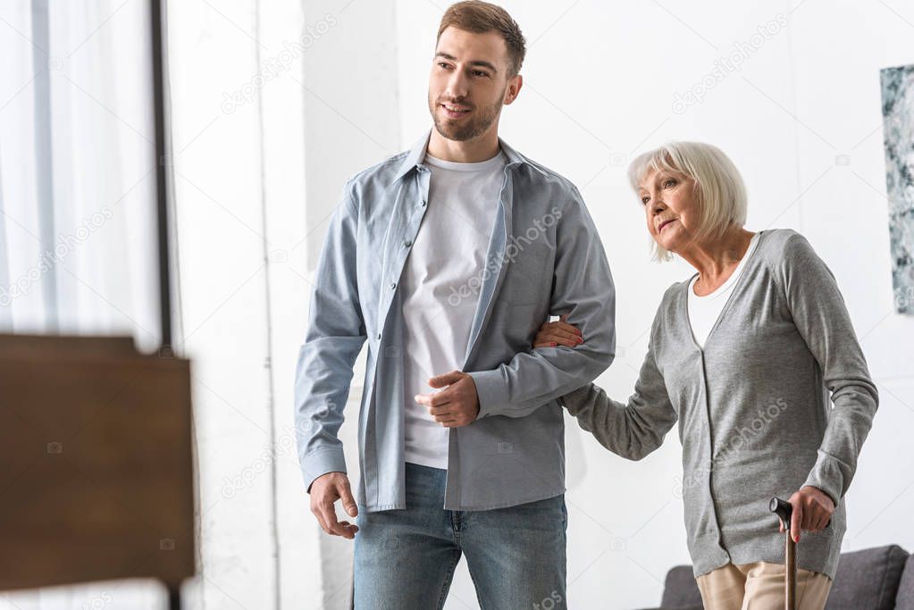 adult son and senior mother with walking stick at home