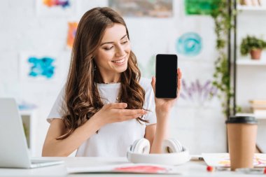 Boş ekranlı akıllı telefonu elle işaret eden gülümseyen genç kadın. 